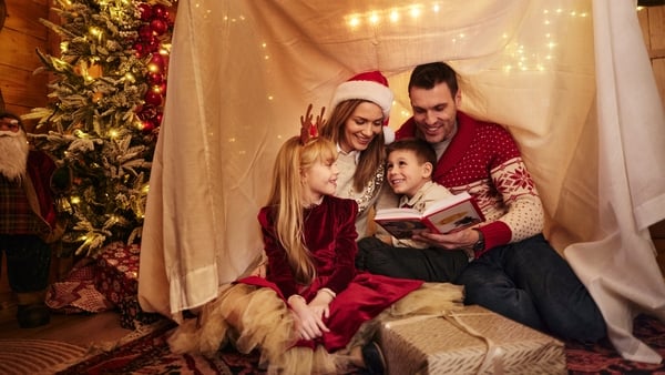 Happy parents and their small kids reading a book while relaxing on Christmas night in the living room.