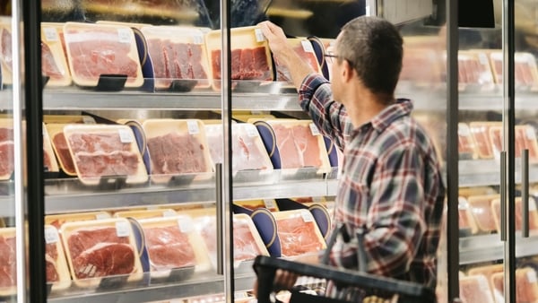 Male customer with a shopping basket taking meat from a fridge at local supermarket