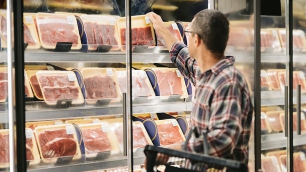 Male customer with a shopping basket taking meat from a fridge at local supermarket