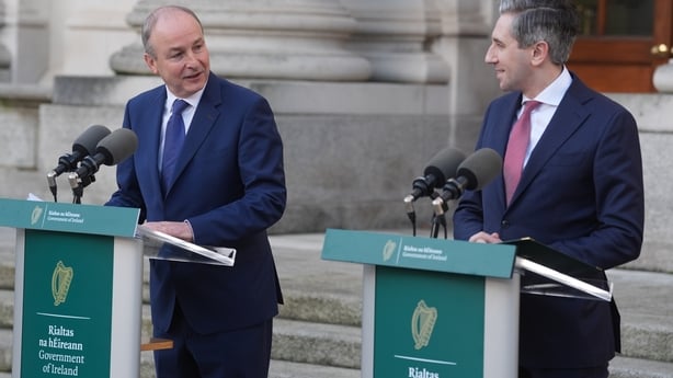 Taoiseach Micheal Martin and Tanaiste Simon Harris chat as they stand at podiums