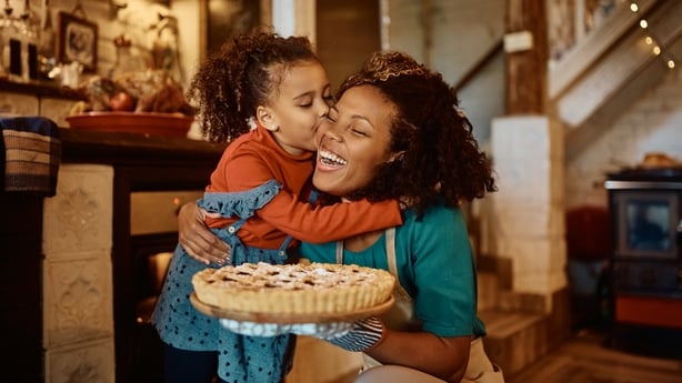 African American mother getting a kiss from her daughter after baking sweet pie in the kitchen.