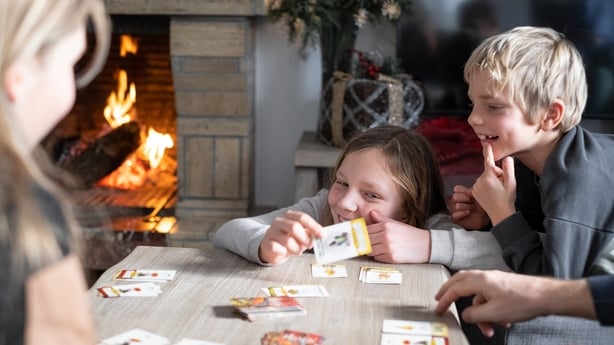 Portraits of smiling and laughing Siblings playing tabletop game at home with Christmas decorations and fire in a chimney