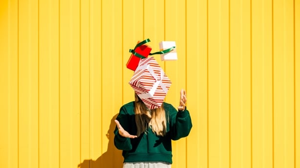 Woman in Christmas hat and green sweater catching Christmas gift boxes against the yellow wall. 