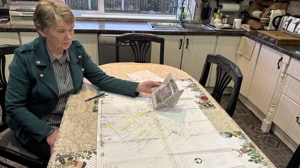 Catherine Corless sit at a kitchen table that has a map on it.