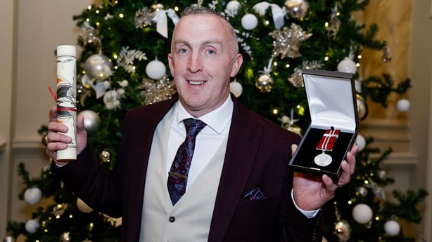 Donal Kavanagh holding up a medal and certificate that he received.
