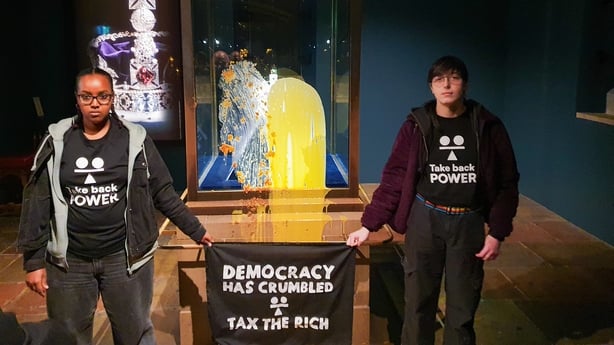 Two supporters of Take Back Power stand beside the Crown Jewels display covered in custard