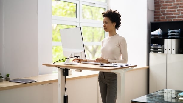 Woman Using Adjustable Height Standing Desk In Office For Good Posture