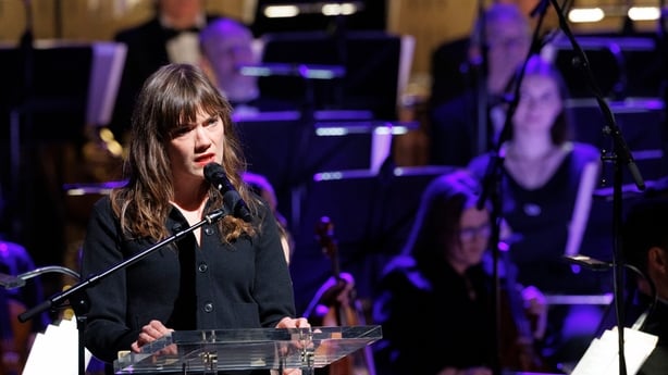 writer Eithne Shortall, with RTÉ Concert Orchestra in background, reads on stage at Sunday Miscellany Christmas concert, National Concert Hall, Dec 2025