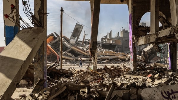 A man carrying walks past destroyed buildings partially covered in murals in the Maghazi refugee camp outside Deir al-Balah