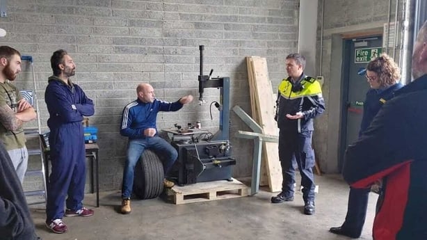 A group of people stand in a semi-circle in a workshop