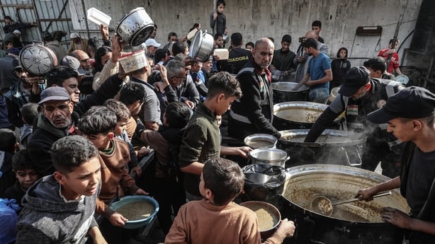 Displaced Palestinians wait to receive hot meal, distributed by a charity organisation, in Gaza