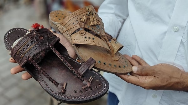 A shopkeeper holds two brown Kolhapuri chappals (handcrafted Indian sandal) in his hands