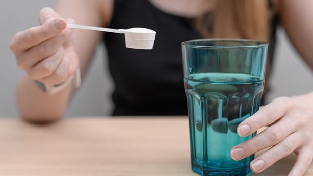 A woman dissolves a scoop of collagen powder in water to drink.