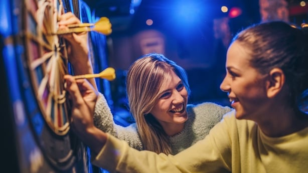 Two female friends having fun while taking darts out of dartboard in a bar.