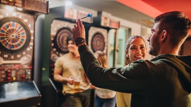 Young smiling couple having fun while playing darts with their friends in a bar.