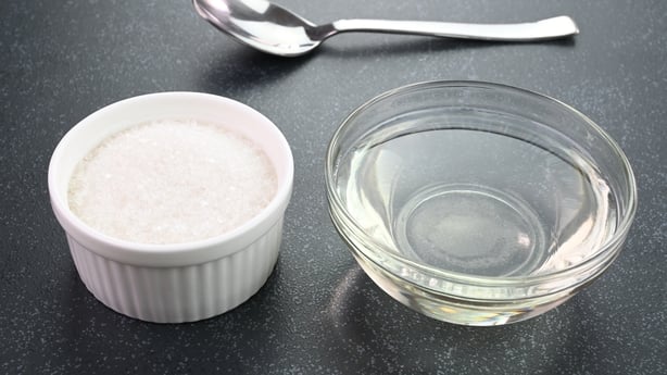 Sugar syrup in a bowl with sugar crystals in the background.