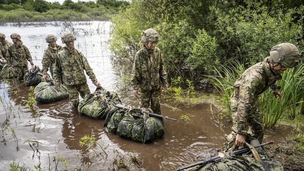 Conscripts from The Royal Life Guards walk through a body of water.
