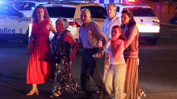 People cross a street next to police vehicles after a shooting incident at Bondi Beach in Sydney
