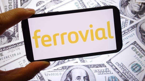 The Ferrovial logo displayed on a smartphone screen with US dollar banknotes in the background