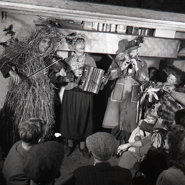 Photograph of a strawboy and two wren boys playing the fiddle accordion and tin whistle at Lios Bui Kilnamartry Macroom Co Cork