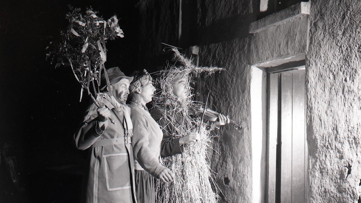 Black and white photograph of a strawboy and two wren boys outside the door at Lios Buí Kilnamartry Macroom Co Cork