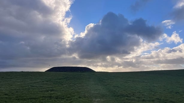 A megalithic stone on a grassy hill with the sun setting behind it