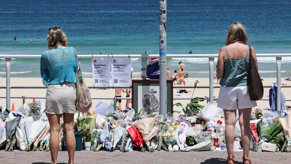 People stand in front floral tributes left at the promenade of Bondi Beach
