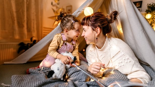 Mother and daughter are having fun reading a book under the illuminated tent in the bedroom.