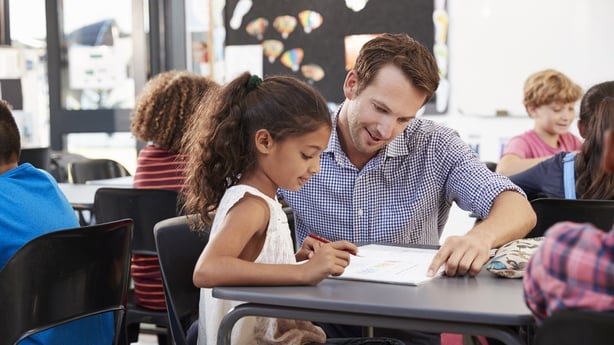 Teacher working with young schoolgirl at her desk in class
