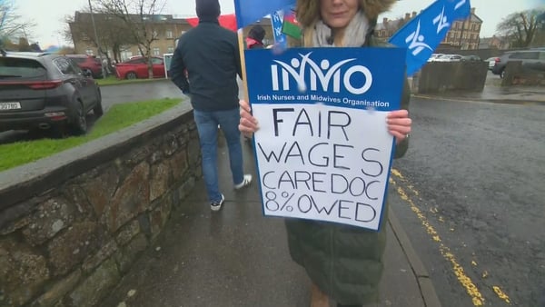 A woman holds a sign in blue and white with the words 'fair wages cardoc 8% owed'