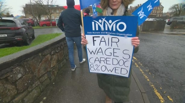 A woman holds a sign in blue and white with the words 'fair wages cardoc 8% owed'