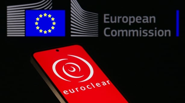 The Euroclear logo is displayed on a mobile phone with the European Commission logo visible in the background in this photo illustration