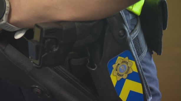 A taser is seen in a holster with a garda logo