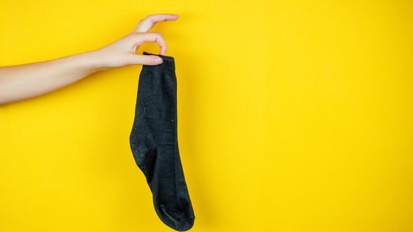 old smelly holey sock in hand on a yellow background