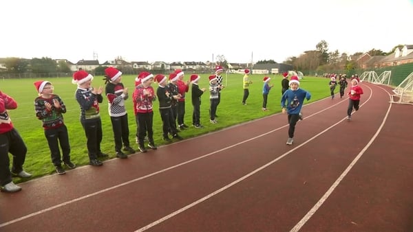 School children run on a race track wearing Santa hats and Christmas jumpers.