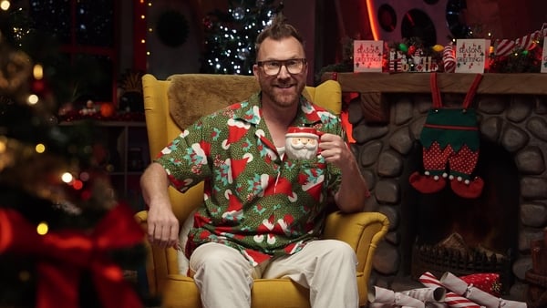 Jason Byrne sits in a seat rasing a cup to say cheers surrounded by Christmas decorations