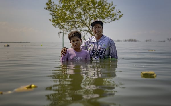 William Gregorio and his son Yamry pose for a portrait where their ancestral home used to stand, now submerged in seawater amid rising tides on August 12, 2025 in Pugad Island, Hagonoy, Philippines