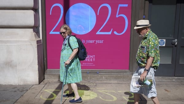 Elderly members of the public walk past a billboard celebrating the year 2025 on Piccadilly, on 12th August 2025, in London, England