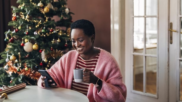 Afro-American woman enjoying her Christmas holiday, drinking coffee and browsing her social media on a mobile phone device.
