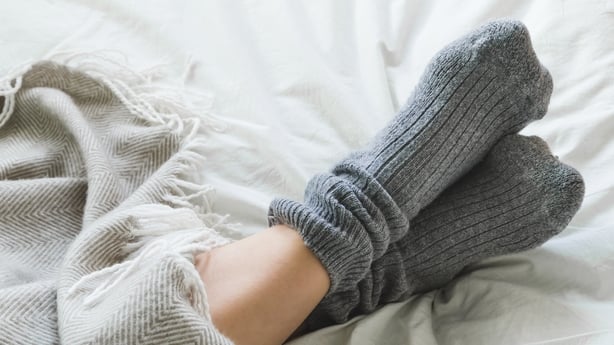 Pair of feet in gray socks on a bed under a cozy blanket.