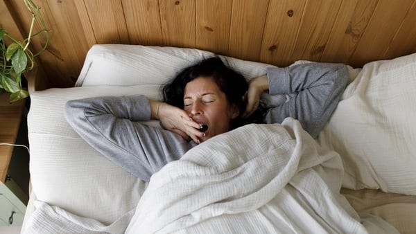 Woman with eyes closed yawning on bed at home