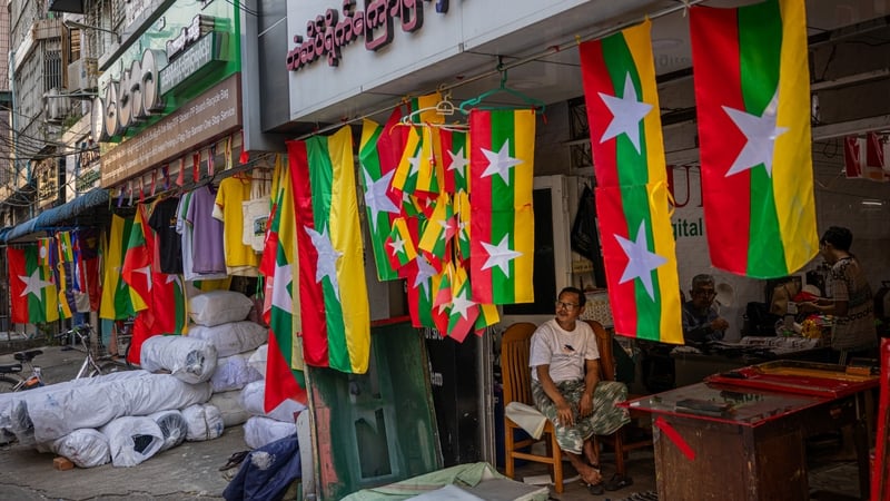 People pass by Myanmar flags hanging outside a screen printing shop in Yangon
