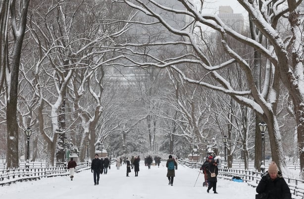 People walk in the snow in Central Park in New York City on December 27, 2025. New York City receieved around 4 inches (10 centimeters) of snow overnight. Airlines canceled 1,500 US flights during the peak holiday travel period Friday, with severe winter storm warnings and heavy snow forecast across