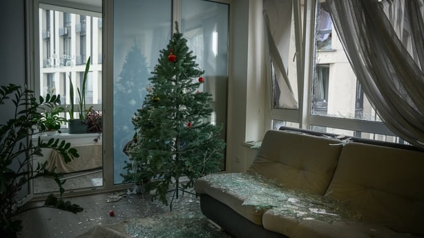 A christmas tree is seen in a damaged apartment with broken glass strewn around 