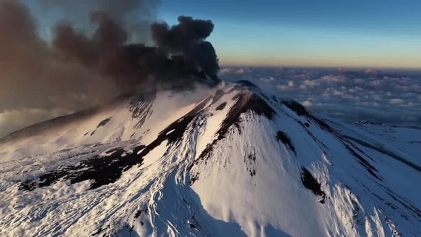 Volcanic ash spews out of an active volcano covered in snow