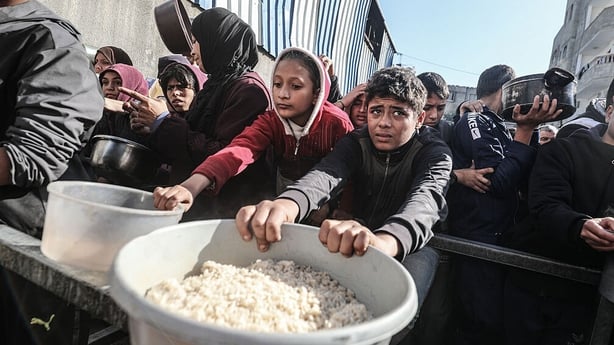 Palestinians, including children, who are struggling to access food gather to receive hot meals distributed by a charity organisation