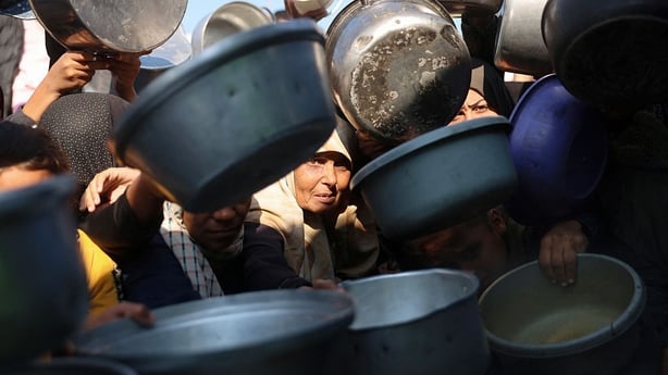 Displaced Palestinians gather to receive donated food portions at a charity kitchen in Khan Yunis 