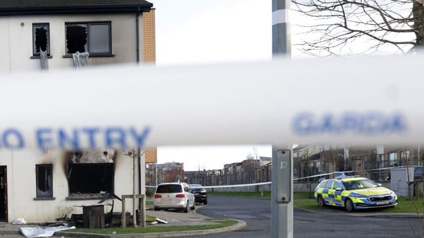 Image shows a garda no entry tape in the foreground with a burned building in the background