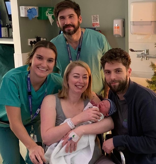 Four adults, two wearing scrubs, and a newborn baby