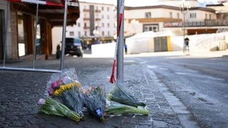 Flowers are laid on a street with police tape in the background
